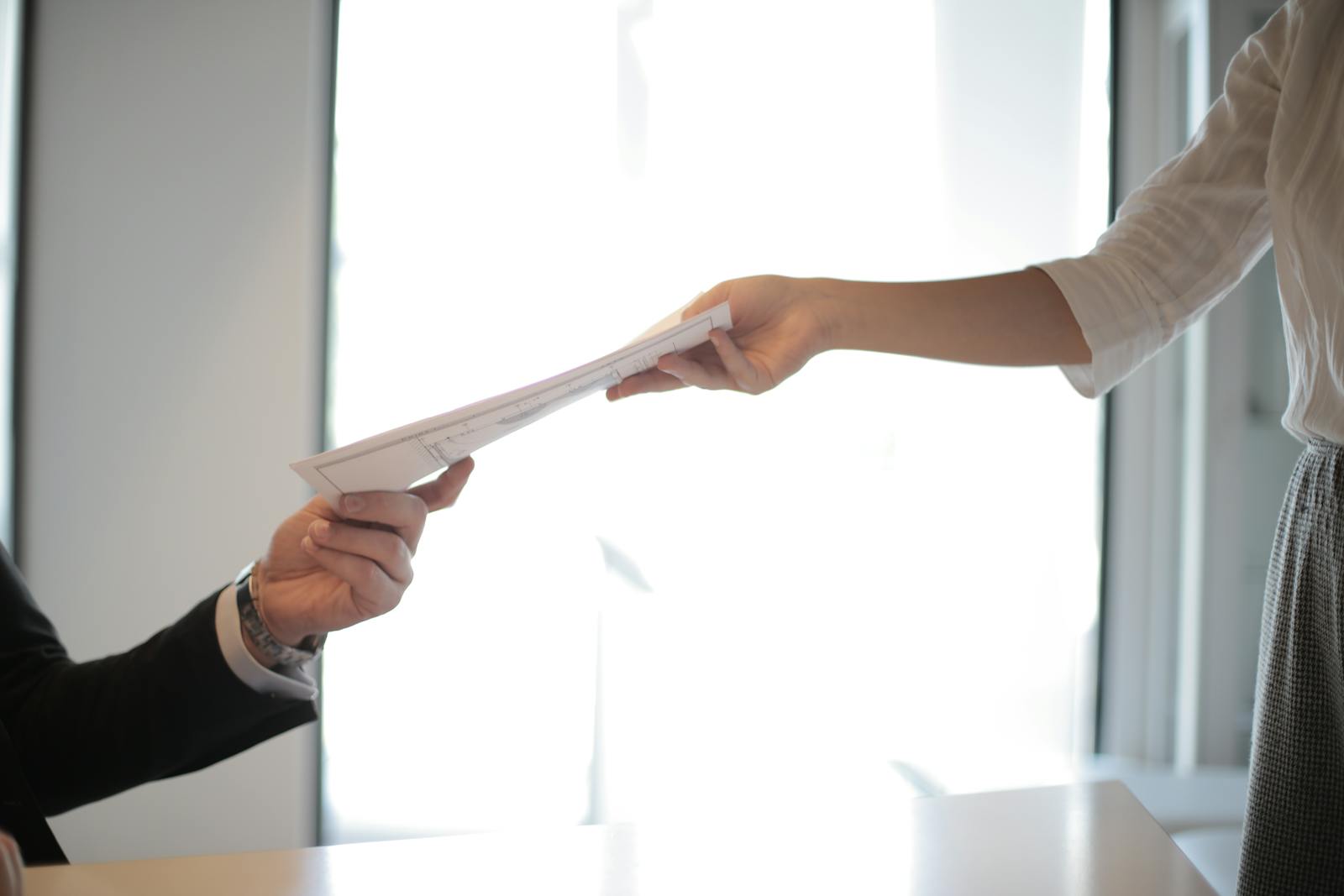 Close-up of hands exchanging documents in a business setting indoors.