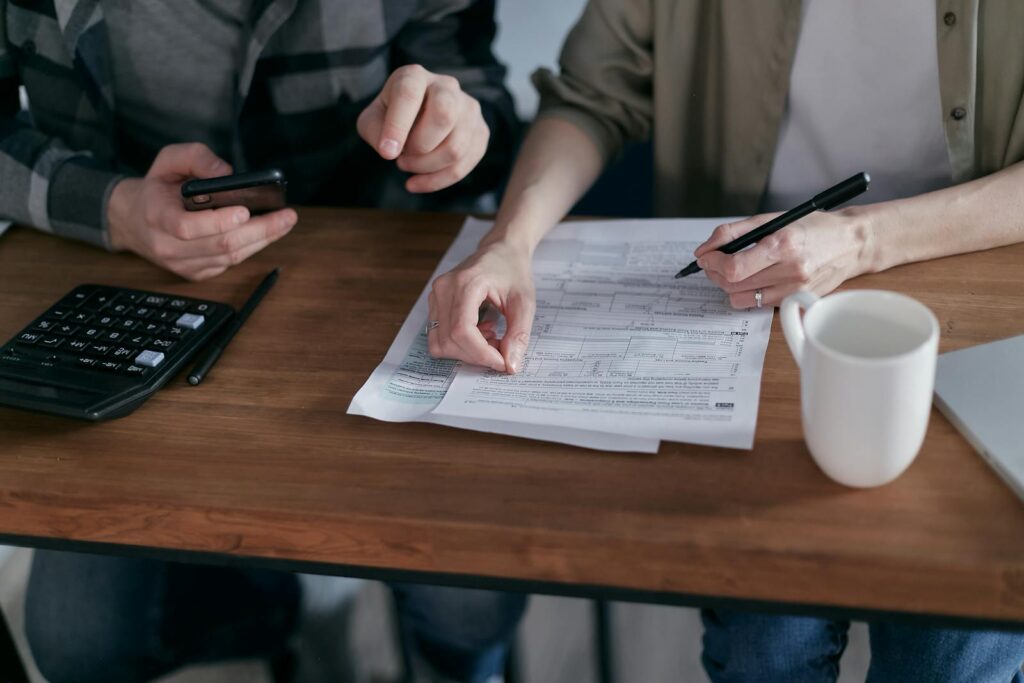 Couple managing finances at home with a calculator, smartphone, and documents.