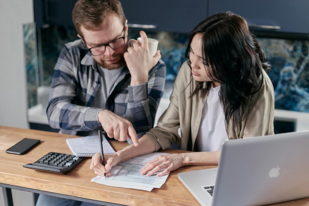 A couple analyzing financial documents with calculator and laptop on a table.