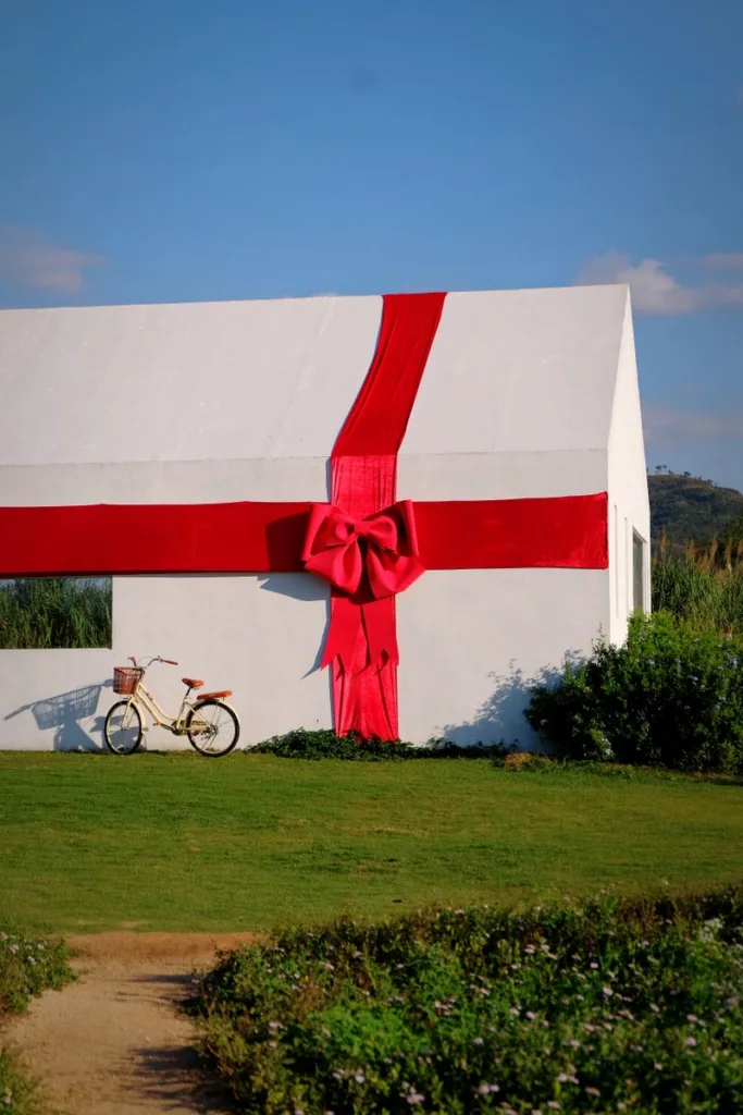 A white house wrapped with a large red ribbon next to a bicycle outdoors.
